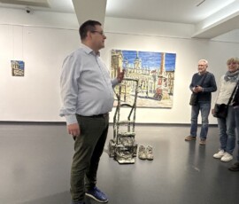 Lehmpfuhls Sackkarre mit Arbeitsschuhen vor dem Bild „Alter Markt in der Mittagssonne"